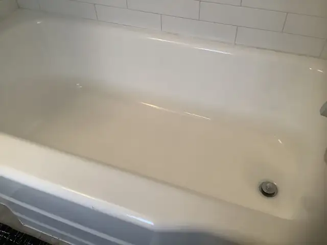 Refinished white bathtub below a white subway tile wall